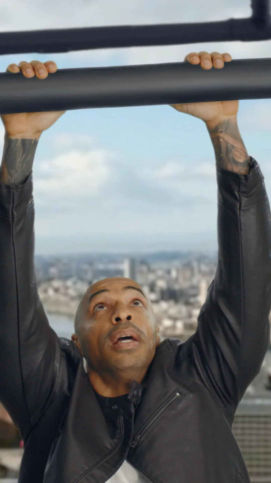 Thierry Henry hanging from a bar high above a city skyline